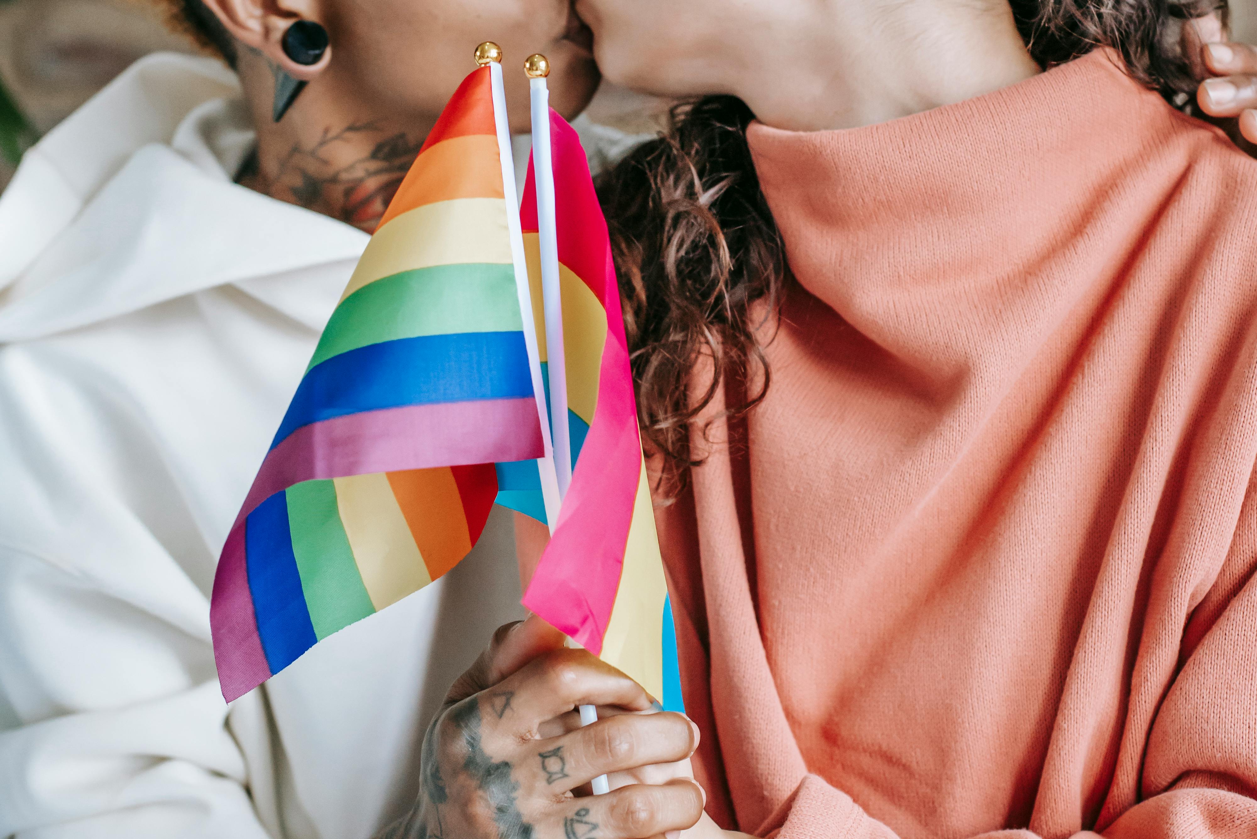 crop faceless lesbian couple kissing and clasping lgbt flags