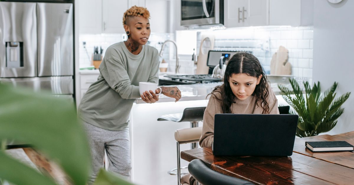 Hispanic woman comparing remittance apps on laptop at home kitchen table