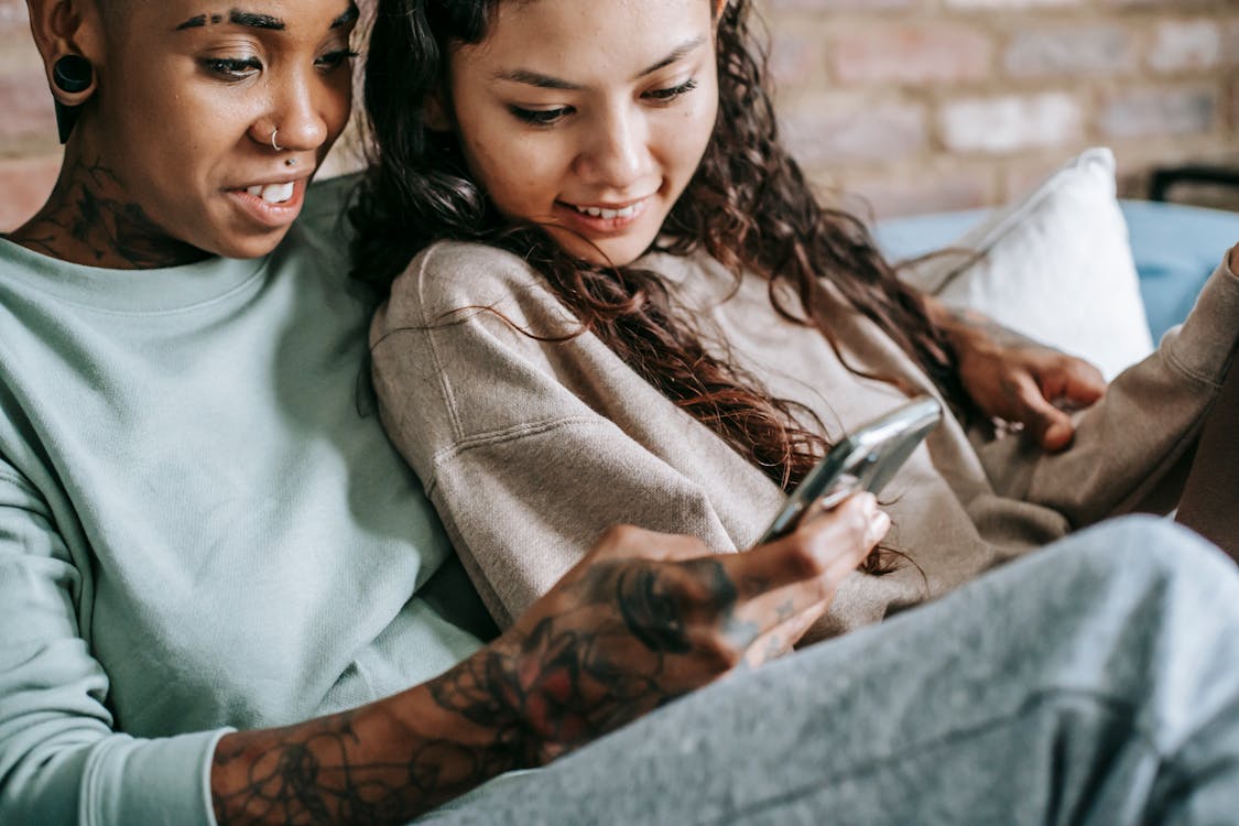 Smiling lesbian couple looking at smartphone on sofa