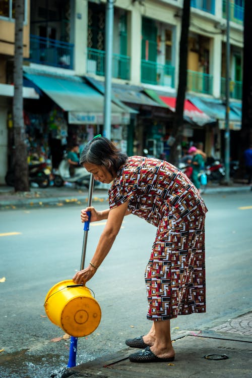 An Elderly Woman Holding a Mop and a Bucket