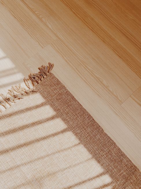 Cozy woven rug on wooden floor with natural light and shadow play creating a warm atmosphere.