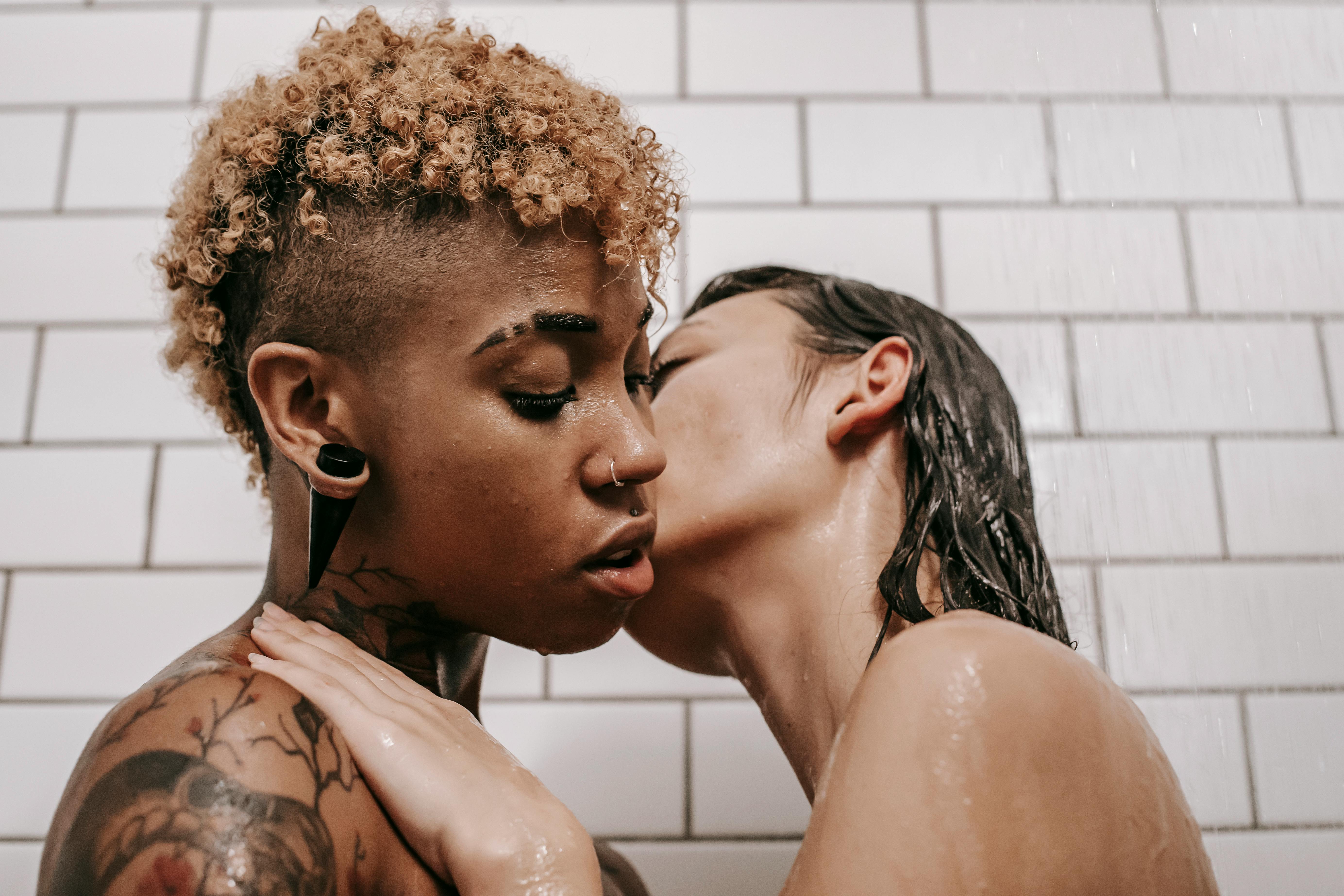multiethnic undressed female couple kissing under shower
