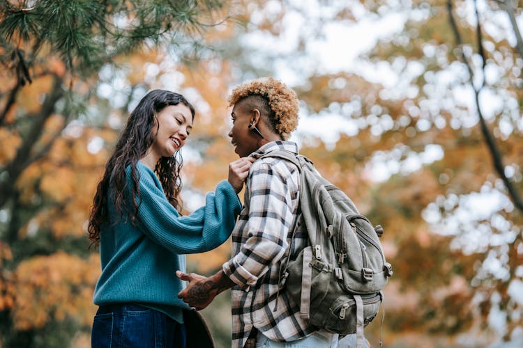 Cheerful Multiethnic Lesbian Couple Standing In Autumn Forest