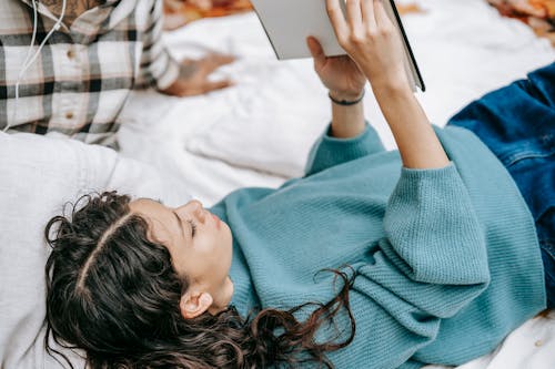 Free From above side view of interested female with book lying on blanket near crop person while resting together in nature on autumn day Stock Photo