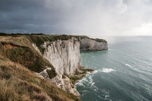 Free Majestic cliffs at Étretat, Normandy, France, under a dramatic cloudy sky. Stock Photo