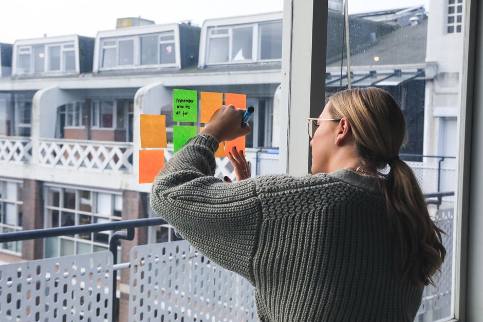 A businesswoman writing notes on sticky notes on a window in an office setting.