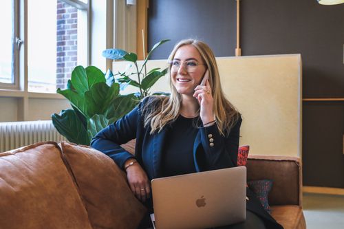 Free Smiling woman working remotely, multitasking with a phone call and laptop in a stylish office. Stock Photo