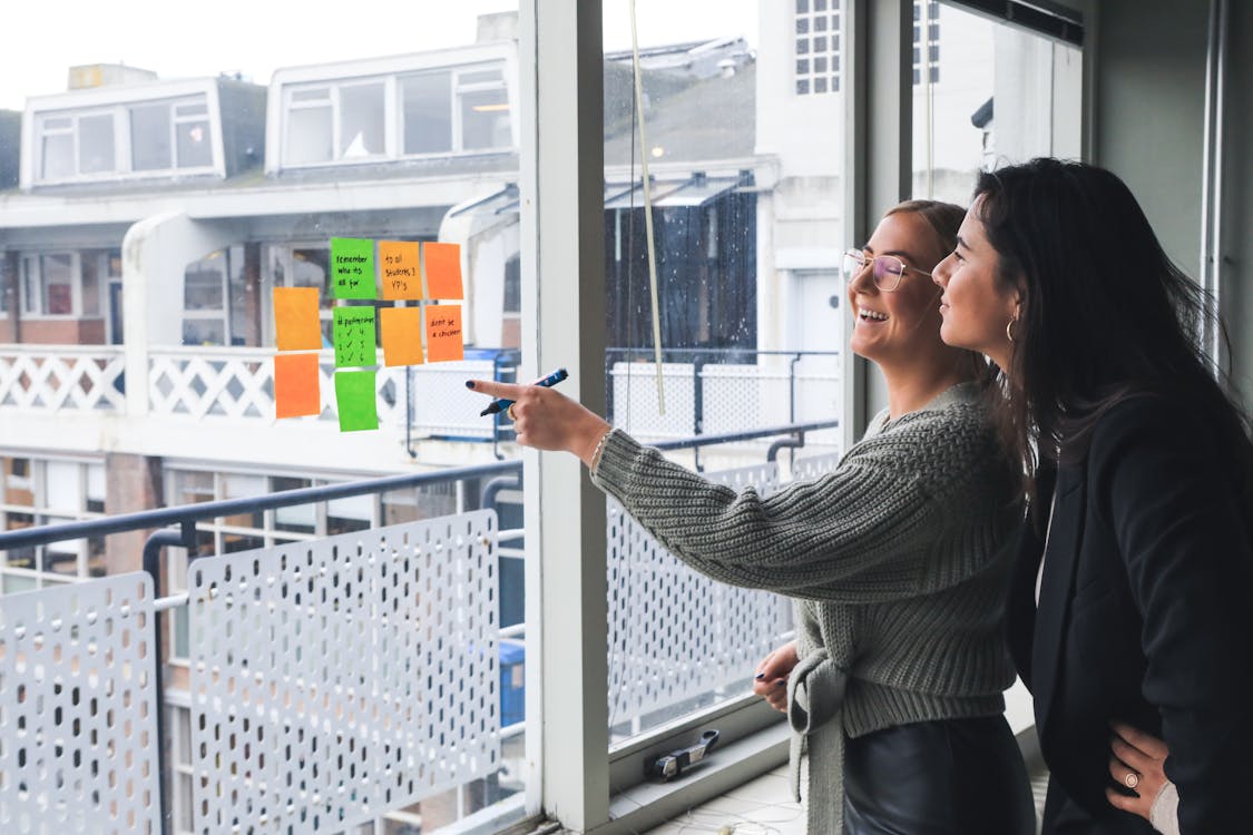 Free Two Women Looking at Sticky Notes on a Glass Window Stock Photo