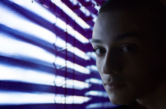 An artistic portrait with dramatic lighting created by neon light through blinds, emphasizing facial features.
