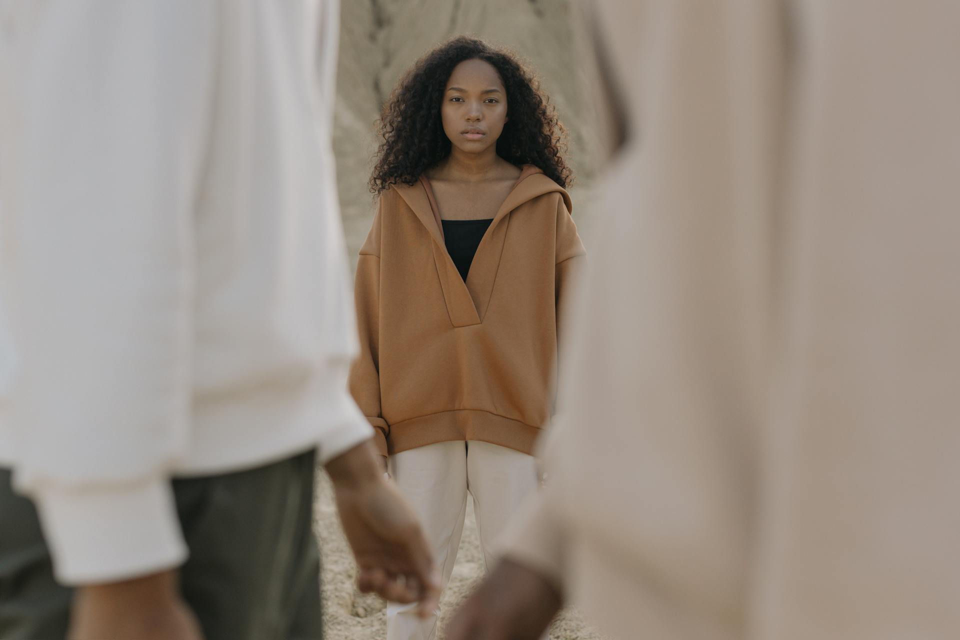 Young woman in brown oversized sweater standing outdoors with soft natural background.