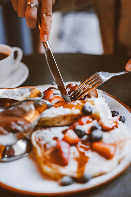 Free Close-up of pancakes topped with fresh berries and syrup, being sliced with a knife and fork. Stock Photo