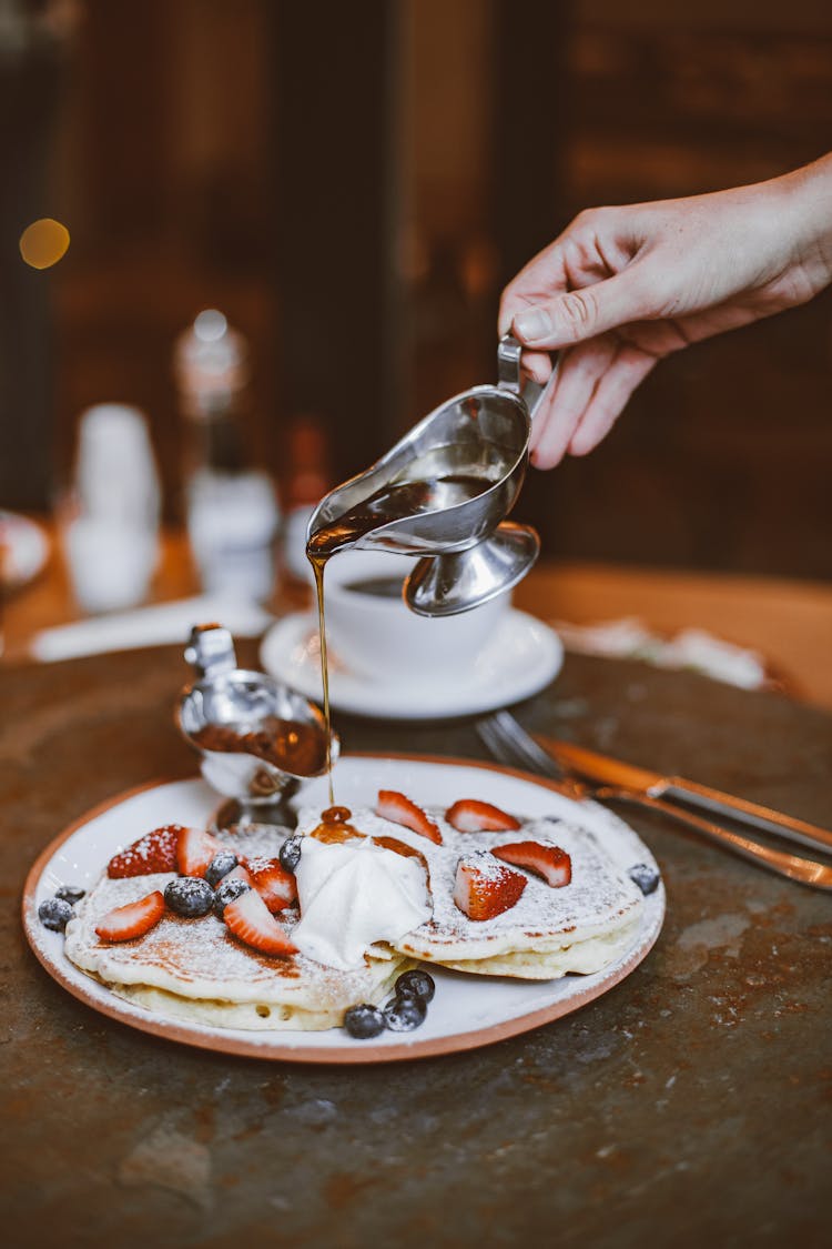 A Person Pouring Honey Syrup On Pancakes