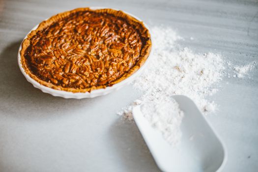Close-up of a freshly baked pecan pie with scattered flour on a marble surface, inviting dessert lovers.