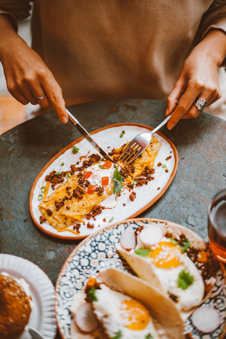 Person Using Fork  And Knife On Food On A Plate