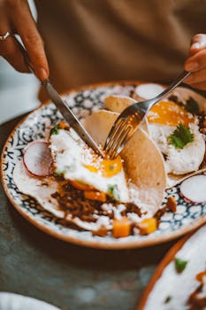 Close-up of hands cutting into a taco with fried egg and vegetables, artistic plating.