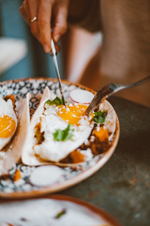 Free Person Holding Stainless Steel Fork and Knife Slicing Cooked Eggs on a Plate Stock Photo