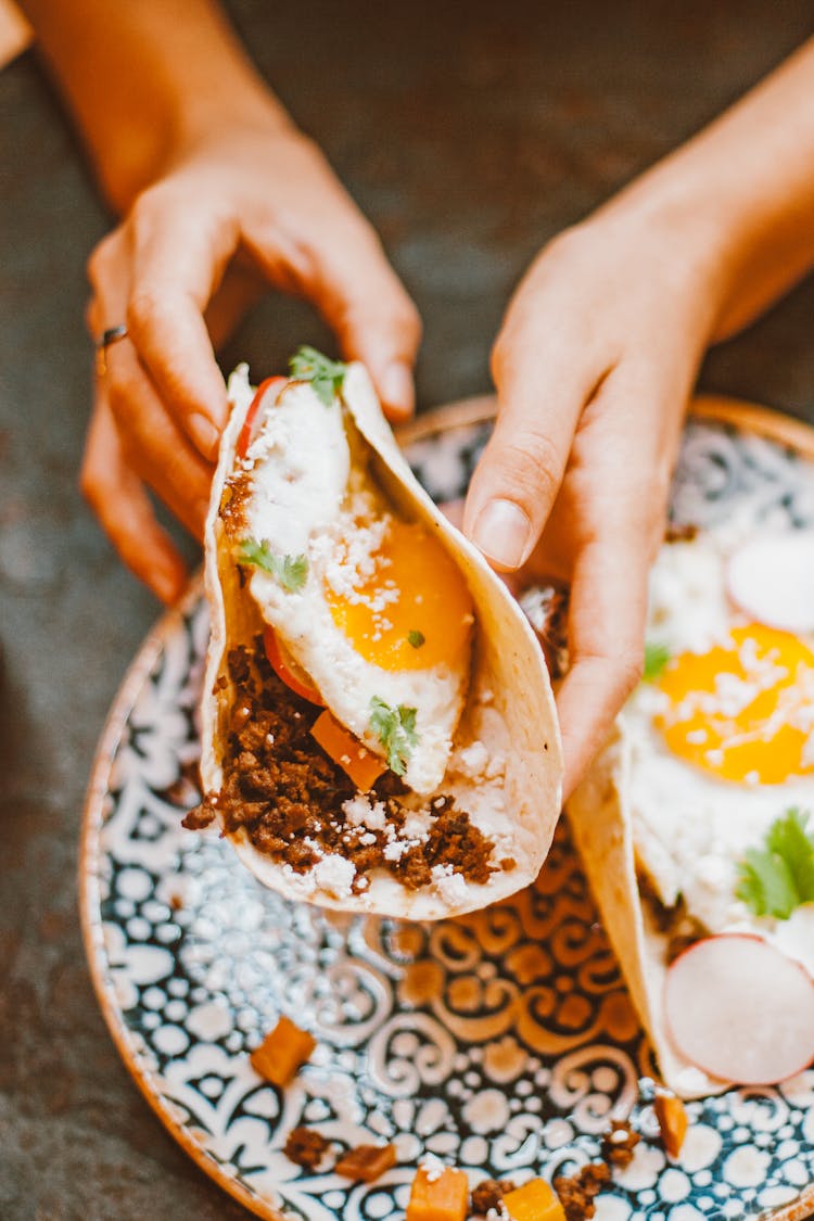 Person Holding A Wrap With Cooked Egg, Meat And Vegetables