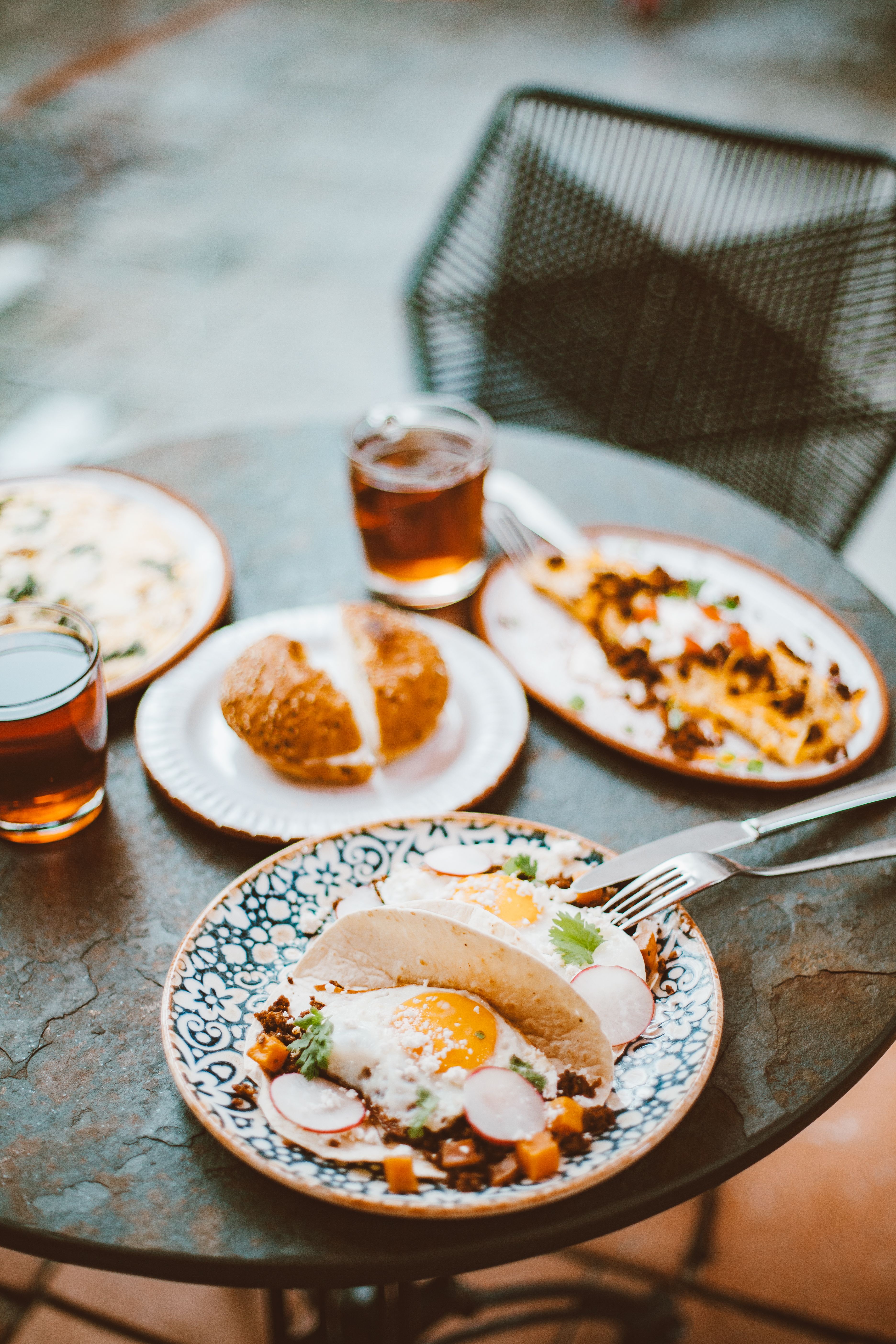Outdoor brunch featuring tacos with fried eggs, iced tea, and fresh bread on a rustic table.