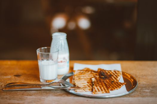A warm breakfast setting with grilled tortilla, milk bottle, and cutlery on a rustic table.