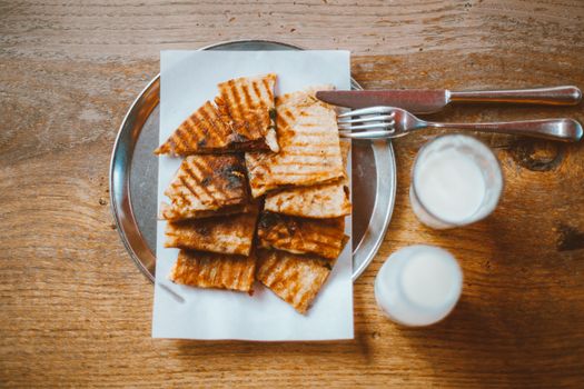 A top view of grilled flatbread on a plate with glasses of milk on a wooden table.