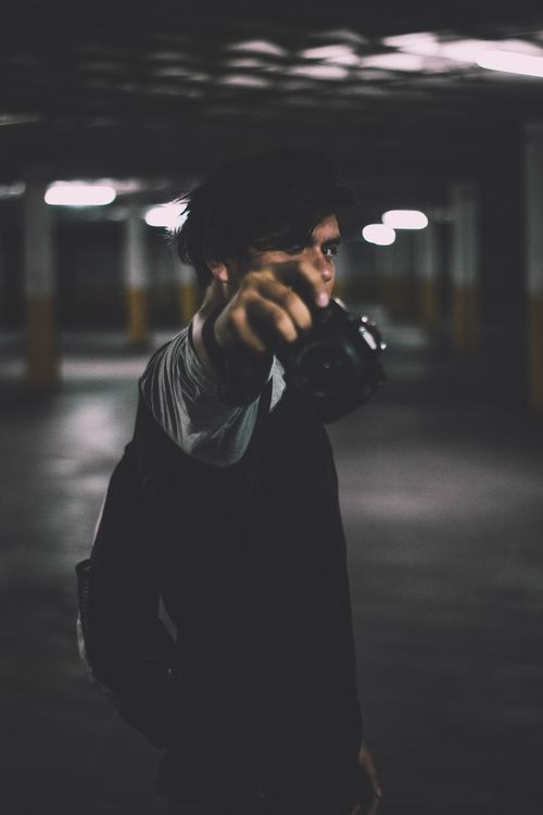Free Moody portrait of a young man holding a camera in a dark urban parking lot. Stock Photo