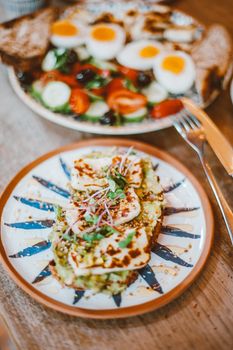 Plate of avocado toast with halloumi and a side of salad featuring boiled eggs.