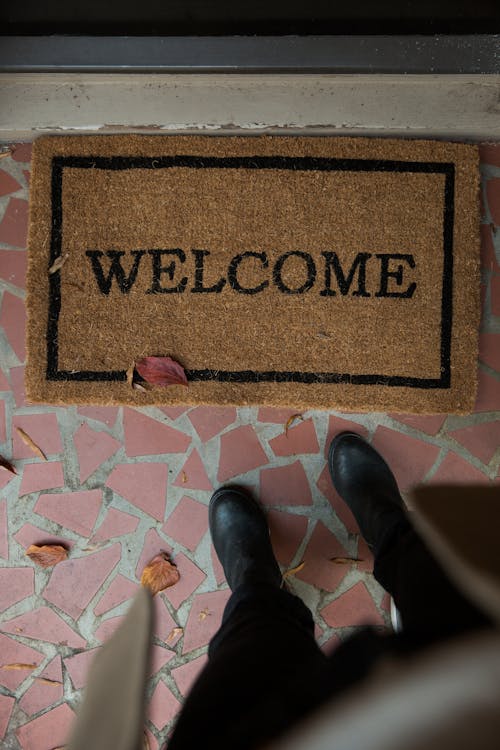 Person Wearing Black Shoes Standing Near a Doormat