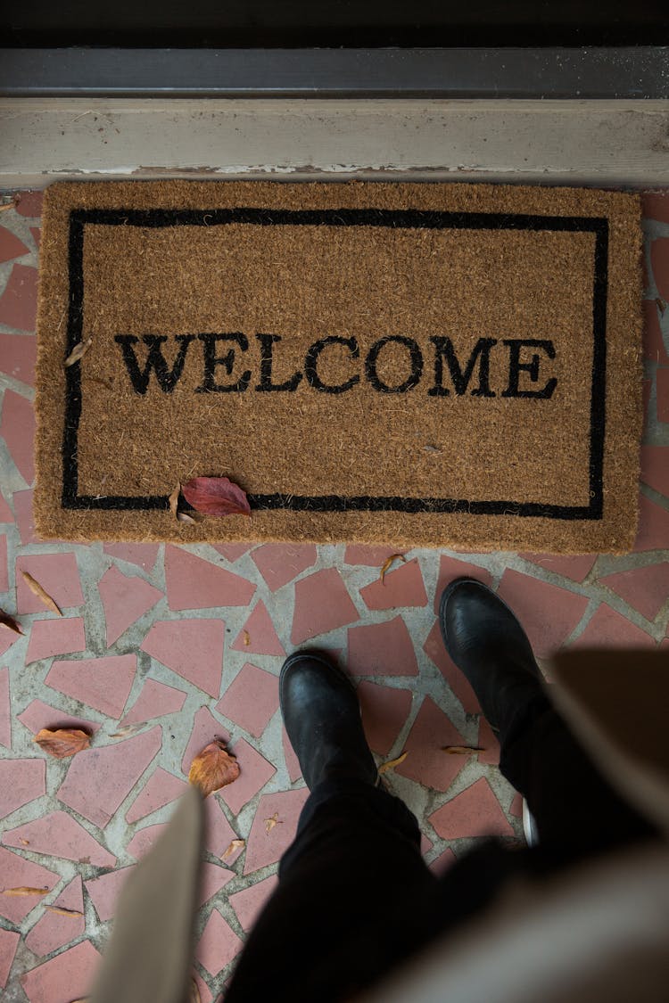 Person Wearing Black Shoes Standing Near A Doormat