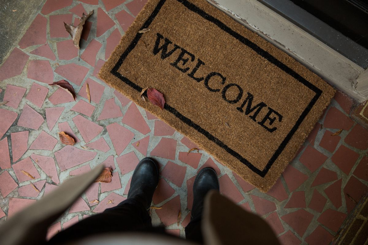 Welcome mat on a tiled porch with boots beside it