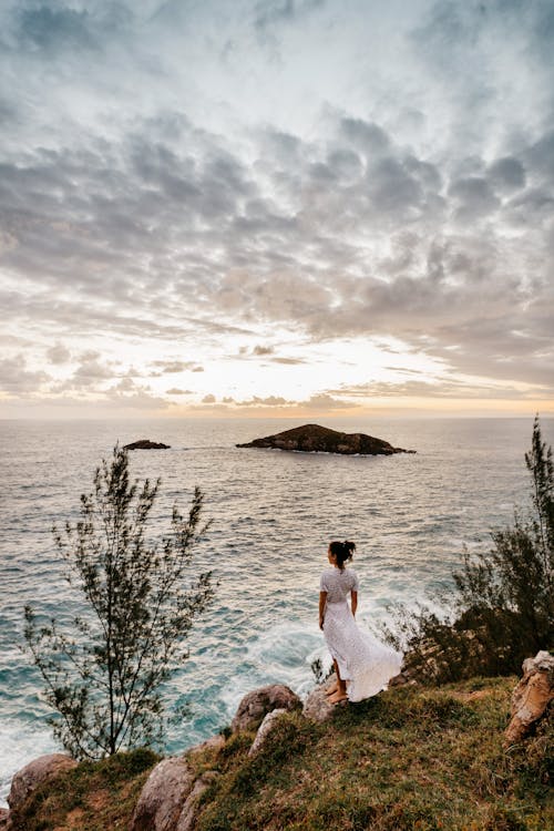 Romantic young woman recreating on rocky seacoast against sunset sky