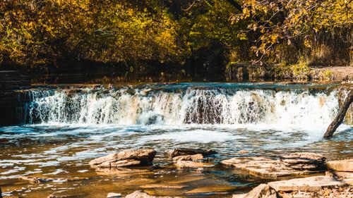 Free A serene waterfall flows gently surrounded by autumn foliage and rocks. Stock Photo