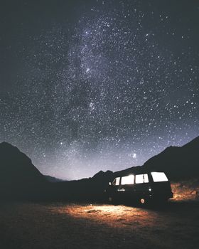 一辆面包车在星空下被照亮，背景是山脉的轮廓