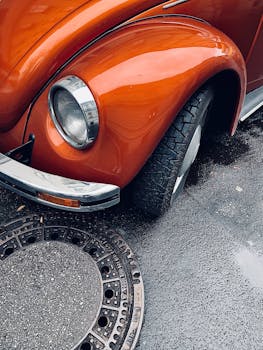 A detailed view of an orange Volkswagen Beetle parked on a wet Berlin street.