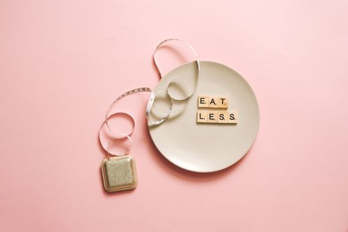 Free A motivational image featuring a plate with scrabble tiles spelling 'Eat Less' on a pink background. Stock Photo