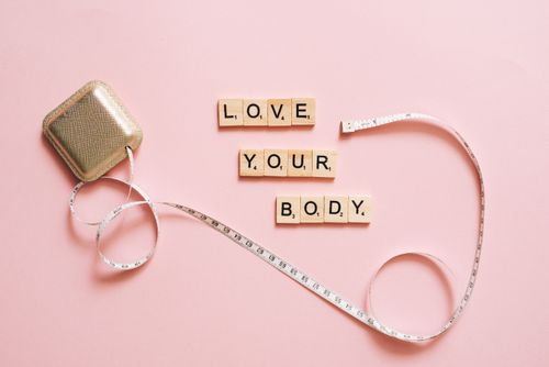 Free Scrabble letters spelling 'Love Your Body' with a tape measure on a pink backdrop. Stock Photo