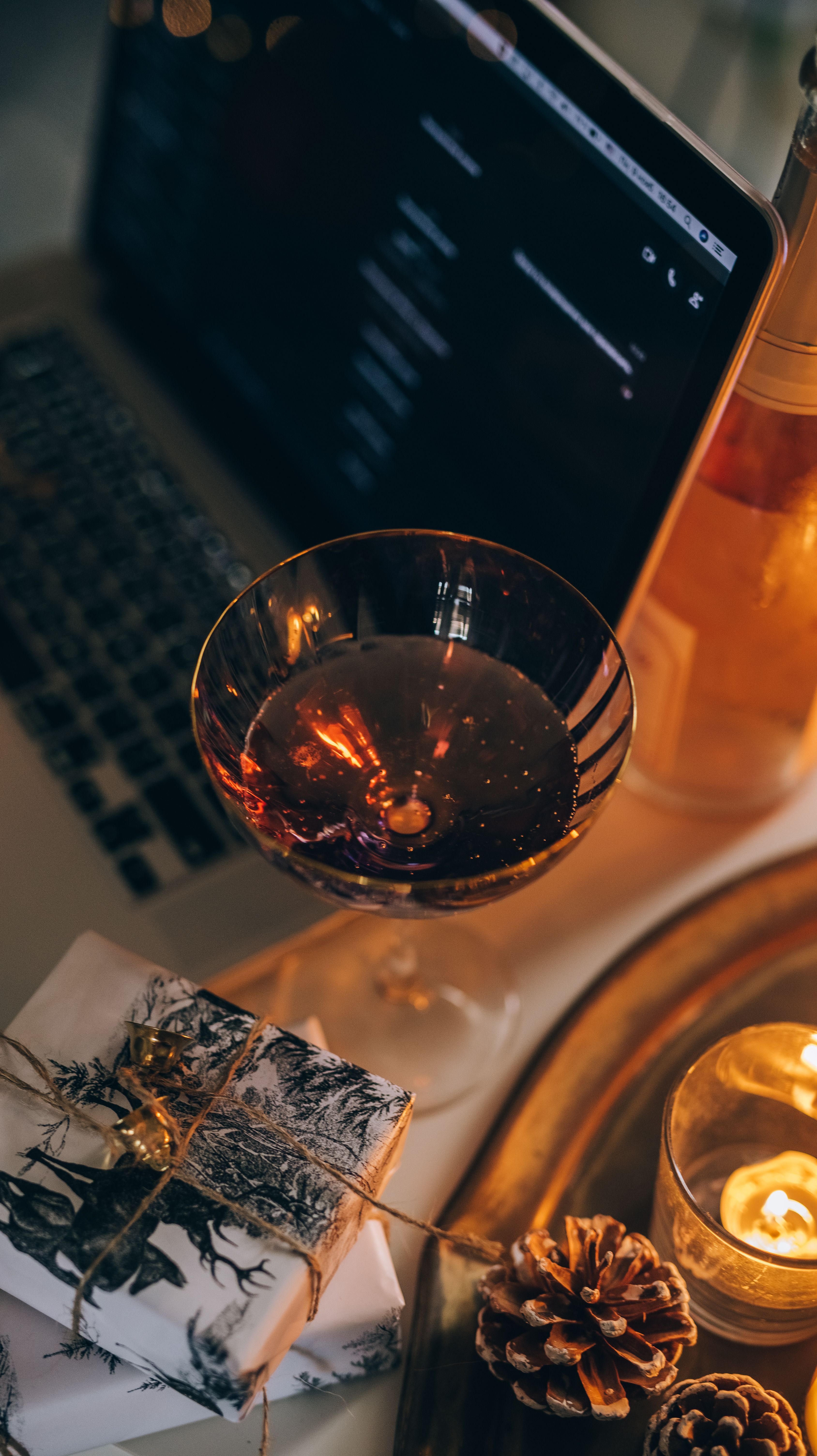A glass of wine, wrapped presents and candles beside an open laptop