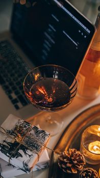 Warm and cozy setup with wine, presents, and candles beside a laptop.