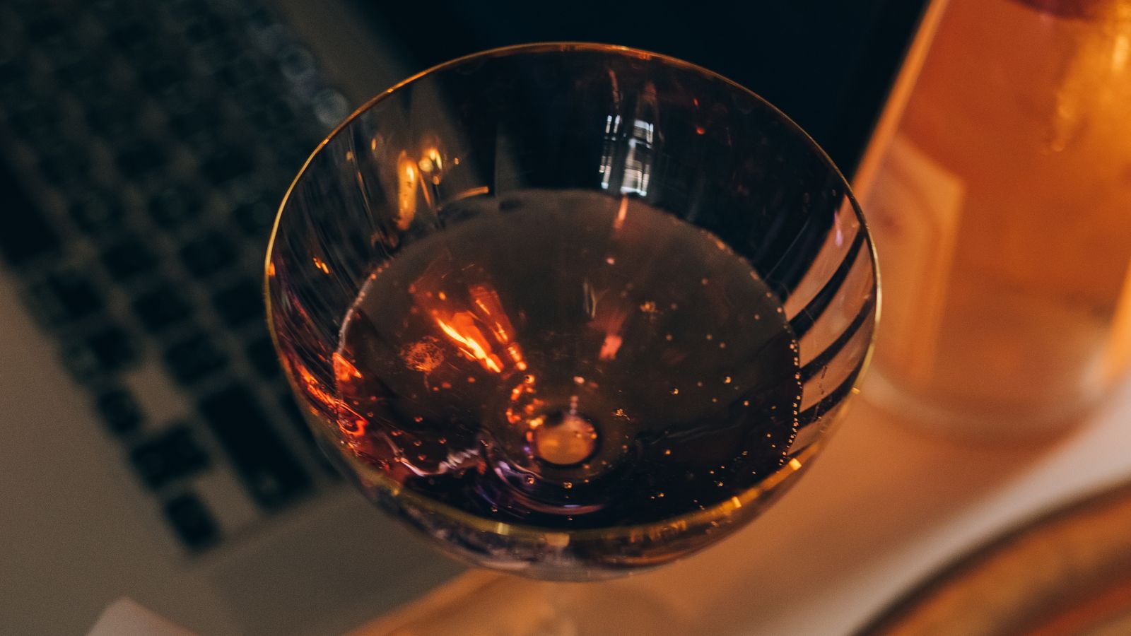 A glass of wine, wrapped presents and candles beside an open laptop