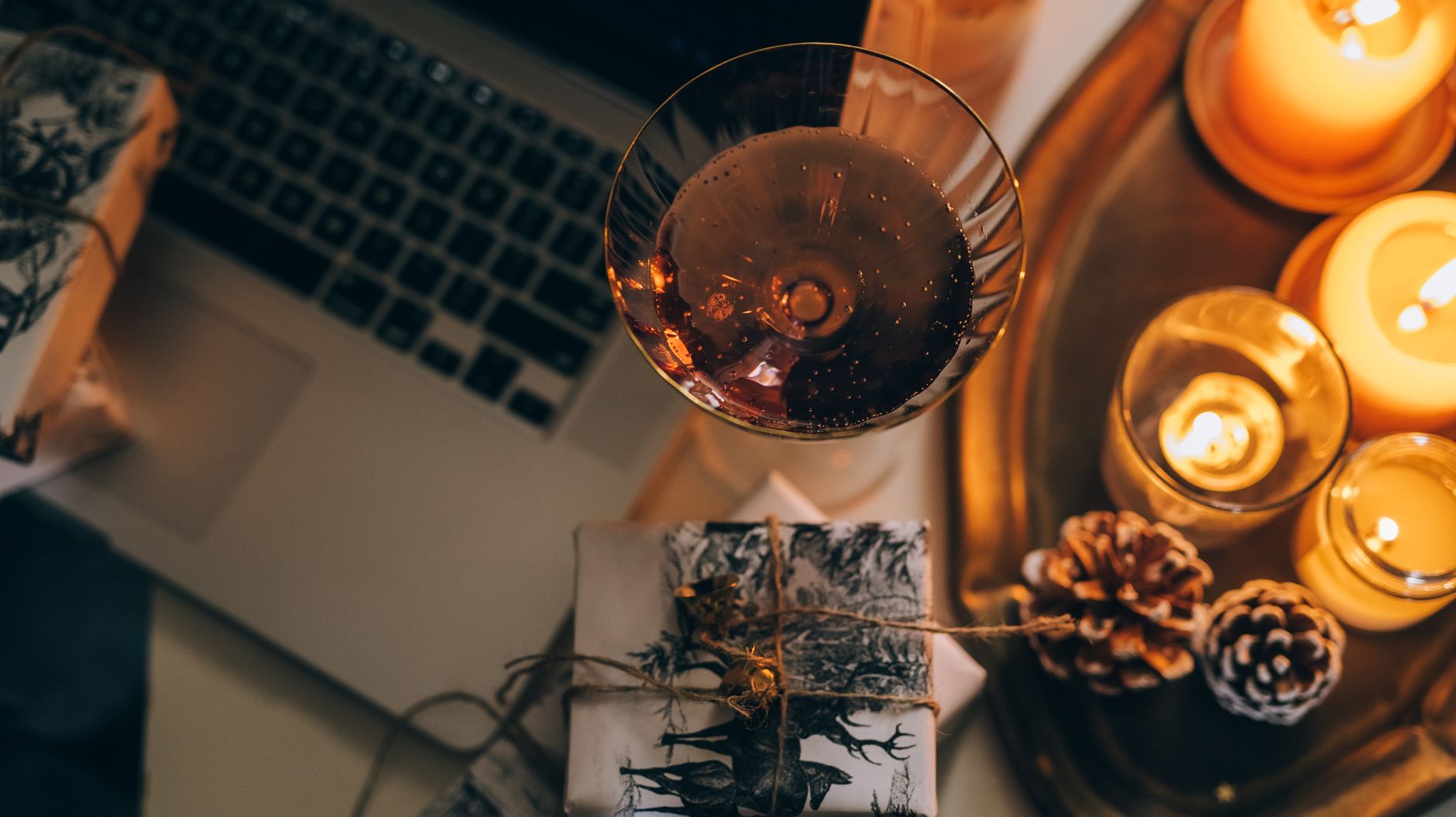 Warm and inviting holiday atmosphere with candles, gifts, and a glass of wine by the laptop.