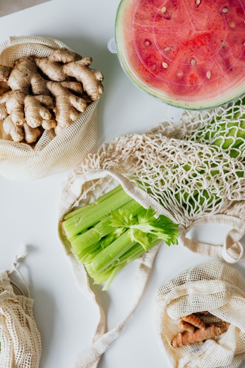 Free Top view of fresh ginger, watermelon, celery, and turmeric in mesh bags on a white counter. Stock Photo