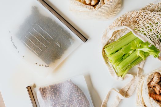 Top view of reusable zip-lock bags and mesh bags with celery and seeds on a white surface.