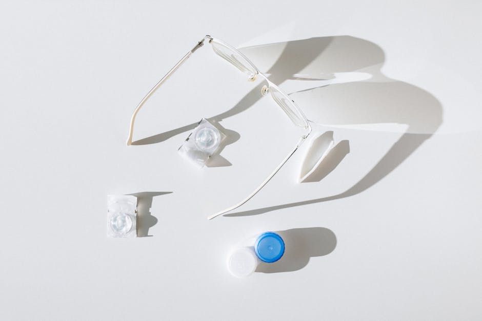 Flat lay of eyeglasses, contact lenses, and case on white background, emphasizing vision care.