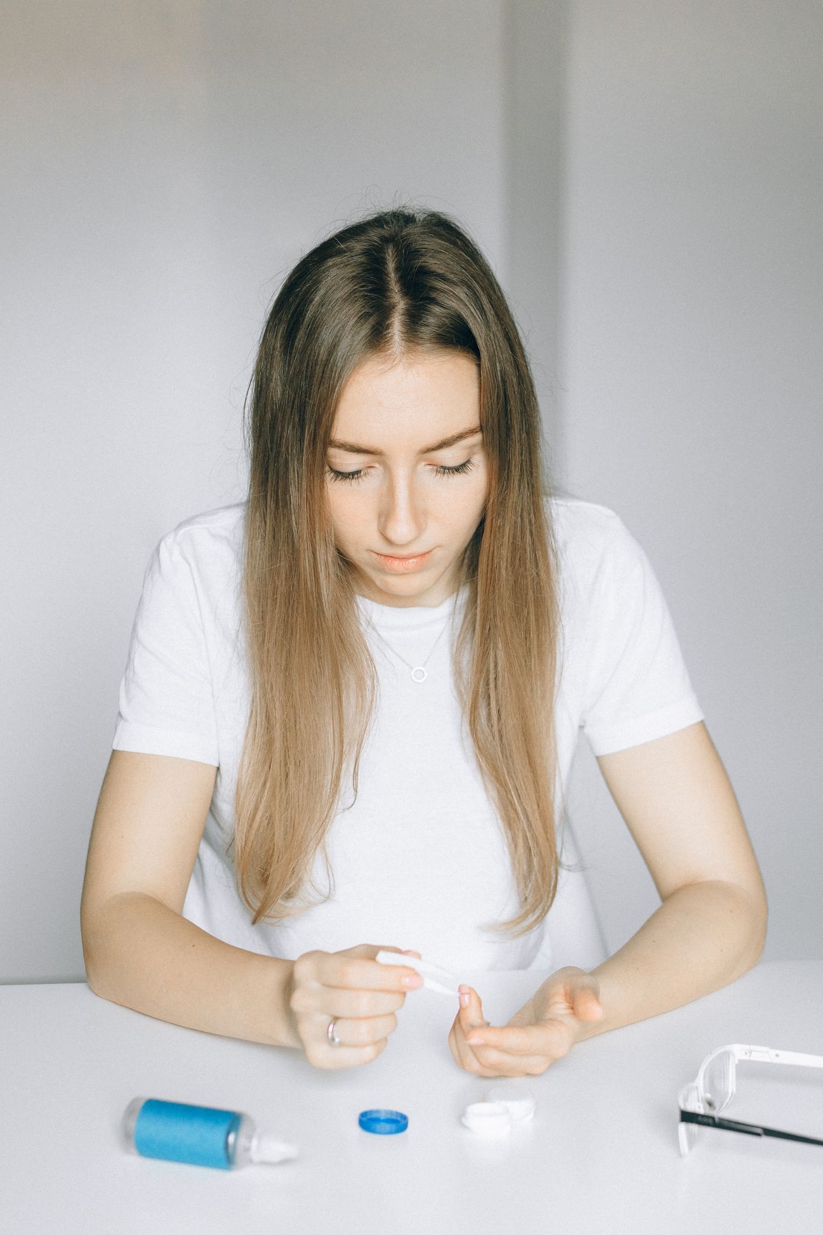 Woman handling contact lenses at a table with lens solution