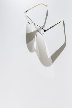 Artistic shot of eyeglasses casting shadows on a white surface, emphasizing minimalist design.