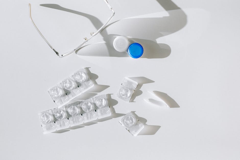 Flatlay of contact lens packages, case, and eyeglasses on a white surface with shadows.