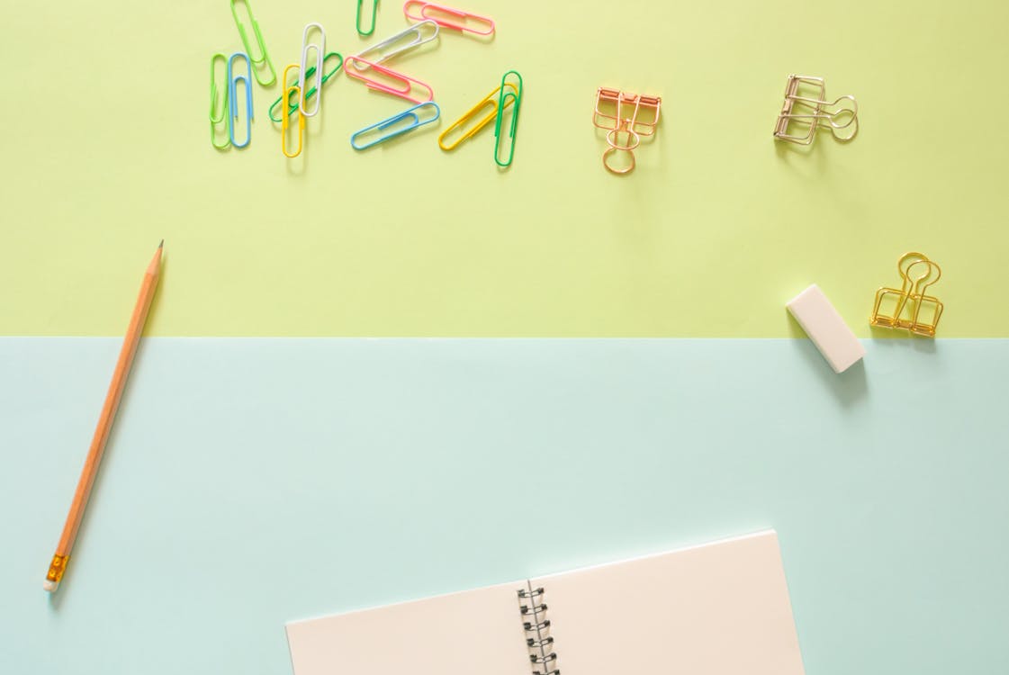 Free Assorted-color Metal Clips on Table Beside Pencil and Notebook Stock Photo