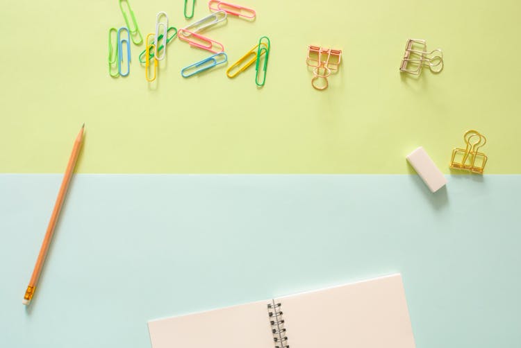 Assorted-color Metal Clips On Table Beside Pencil And Notebook