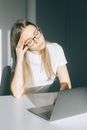 在办公室环境中，一位戴眼镜的年轻女子使用笔记本电脑时感到疲倦