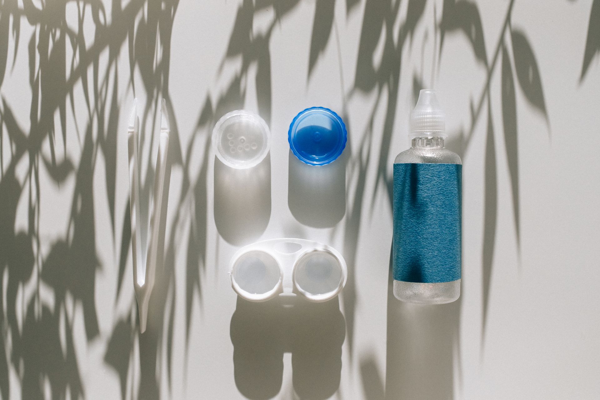 Top view of a contact lens care kit with natural shadows, including solution and tweezers.