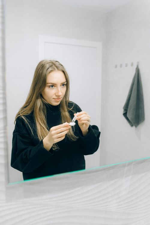 Free A young woman holds a contact lens with care, standing in front of a bathroom mirror. Stock Photo